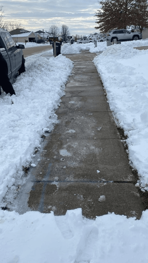 Concrete sidewalk cleared of snow with shoveled piles along both sides